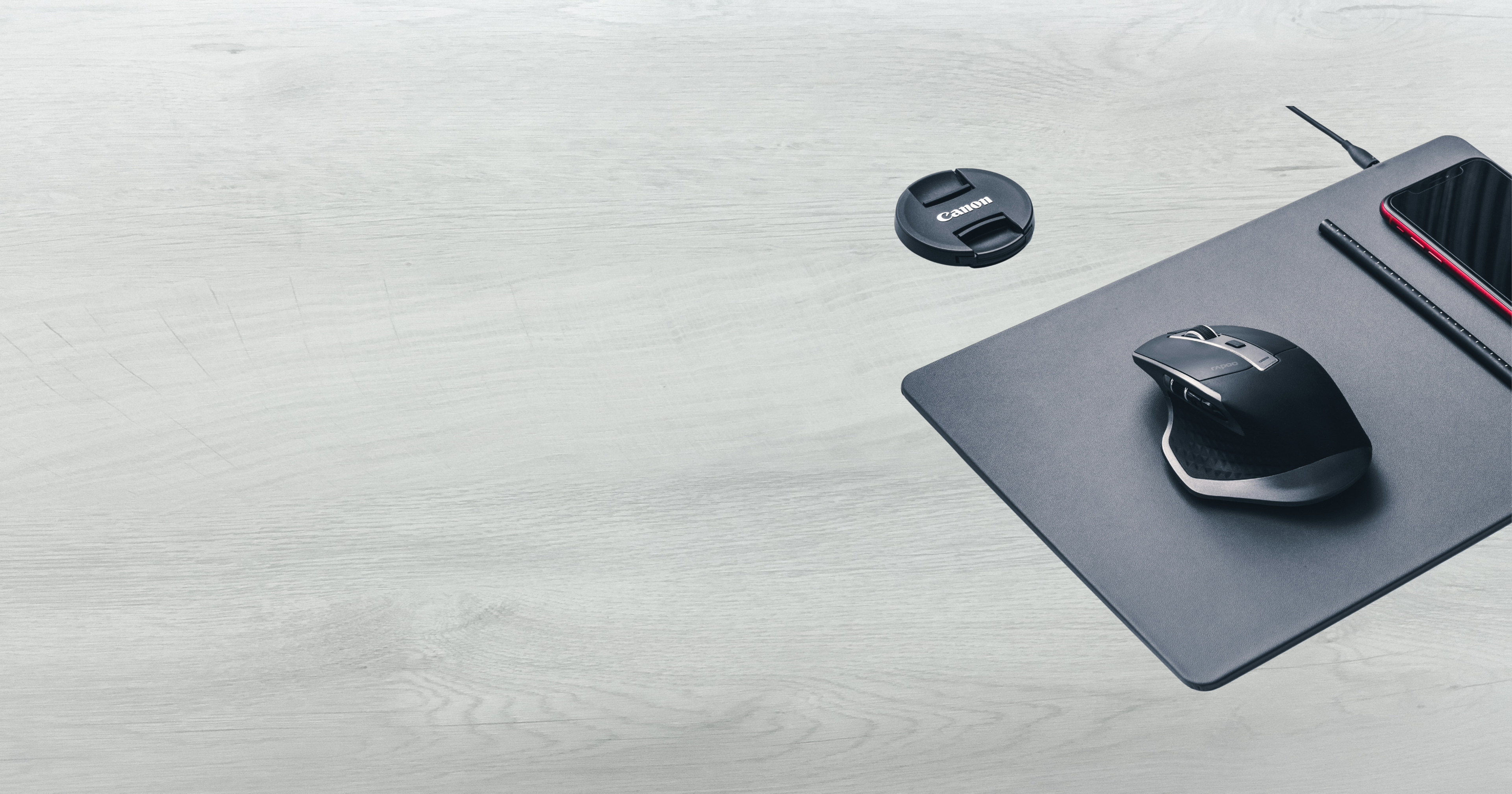 Dessus de bureau avec tapis de souris qui est aussi un chargeur. Dessus, il y a une souris et un iPhone. 